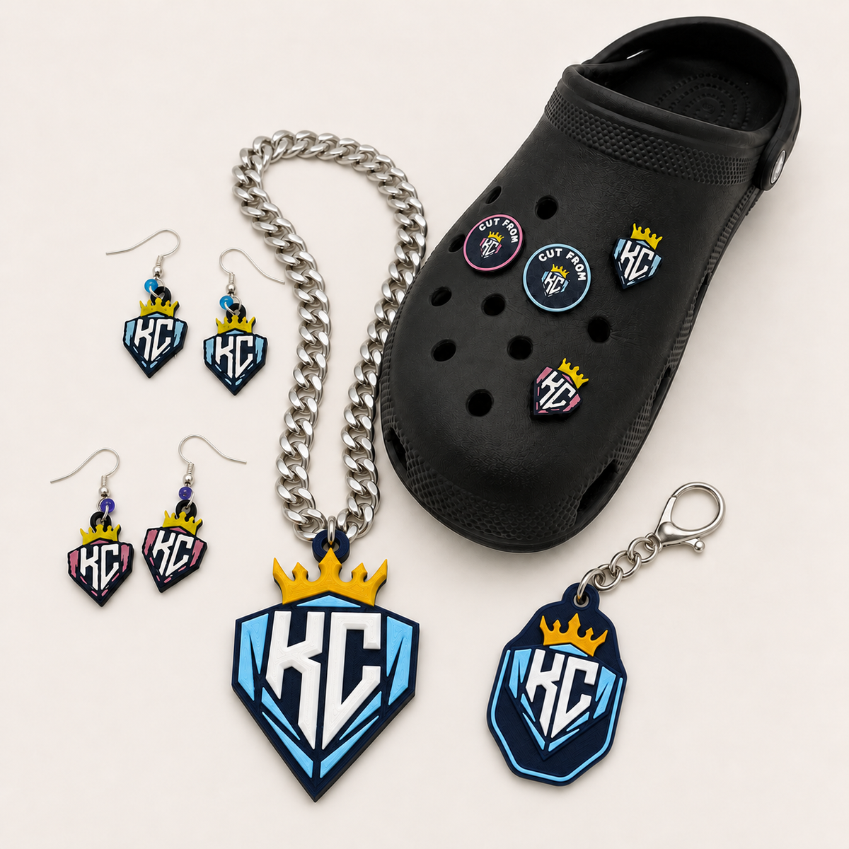 KC Diamonds Team Bundle with the new crowned KC pendant and silver-colored chain, shield keychain with clasp, pink and carolina-blue earrings, and four shoe charms displayed on a black shoe
